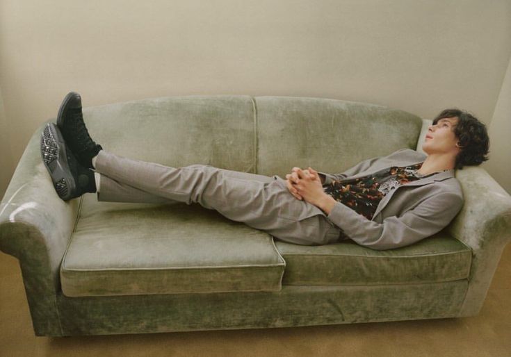 a man laying on top of a green couch with his feet up in the air