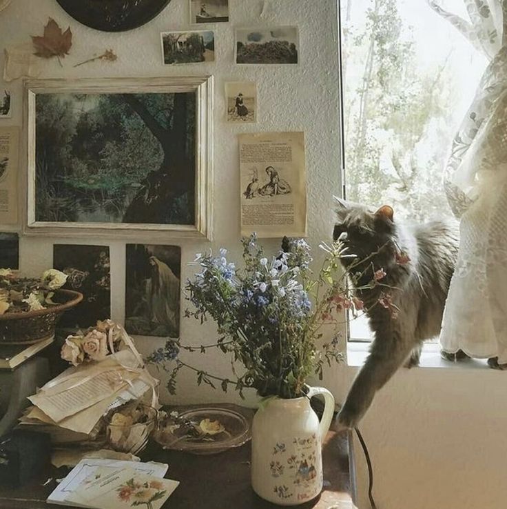 a cat standing on top of a table next to a vase filled with flowers