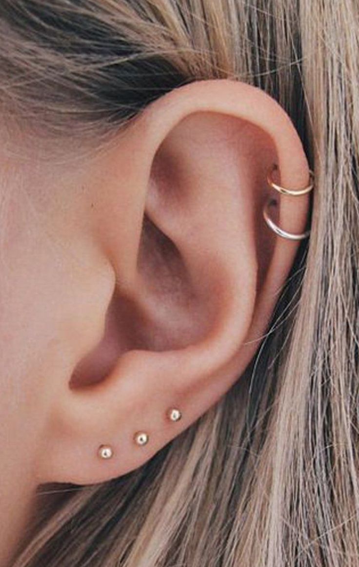 a woman wearing an ear piercing with two small gold dots on the side of her ear