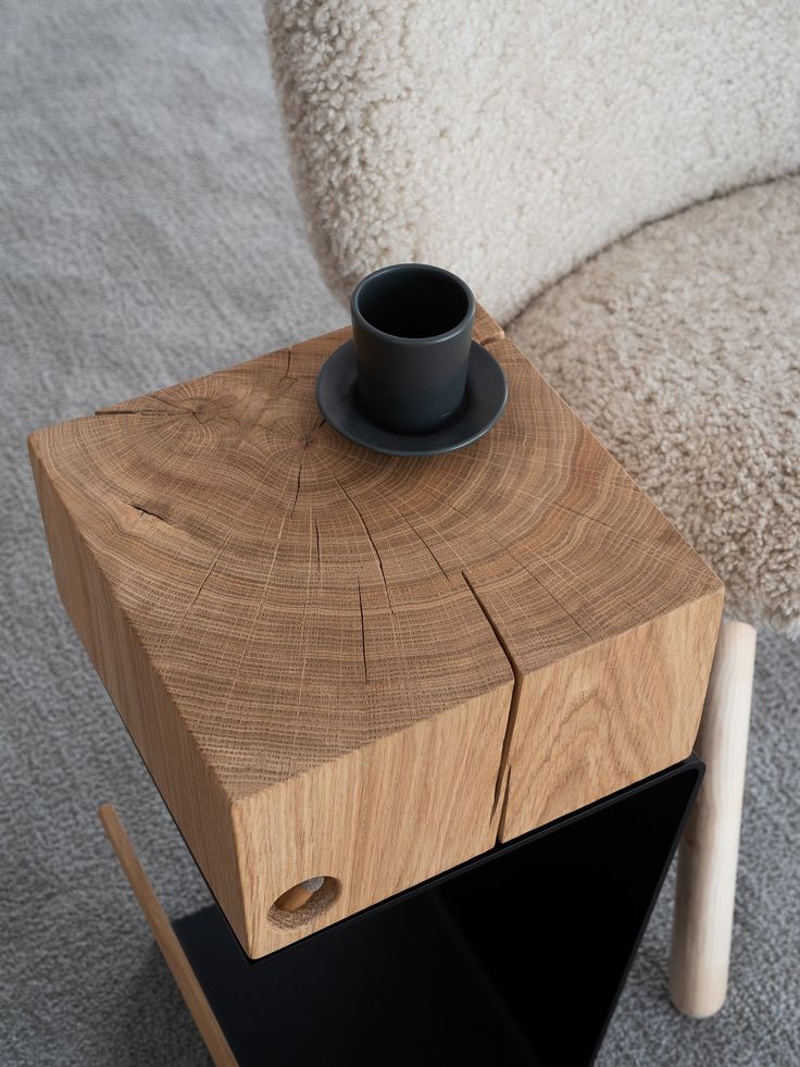 a black cup sitting on top of a wooden table next to a white chair and rug