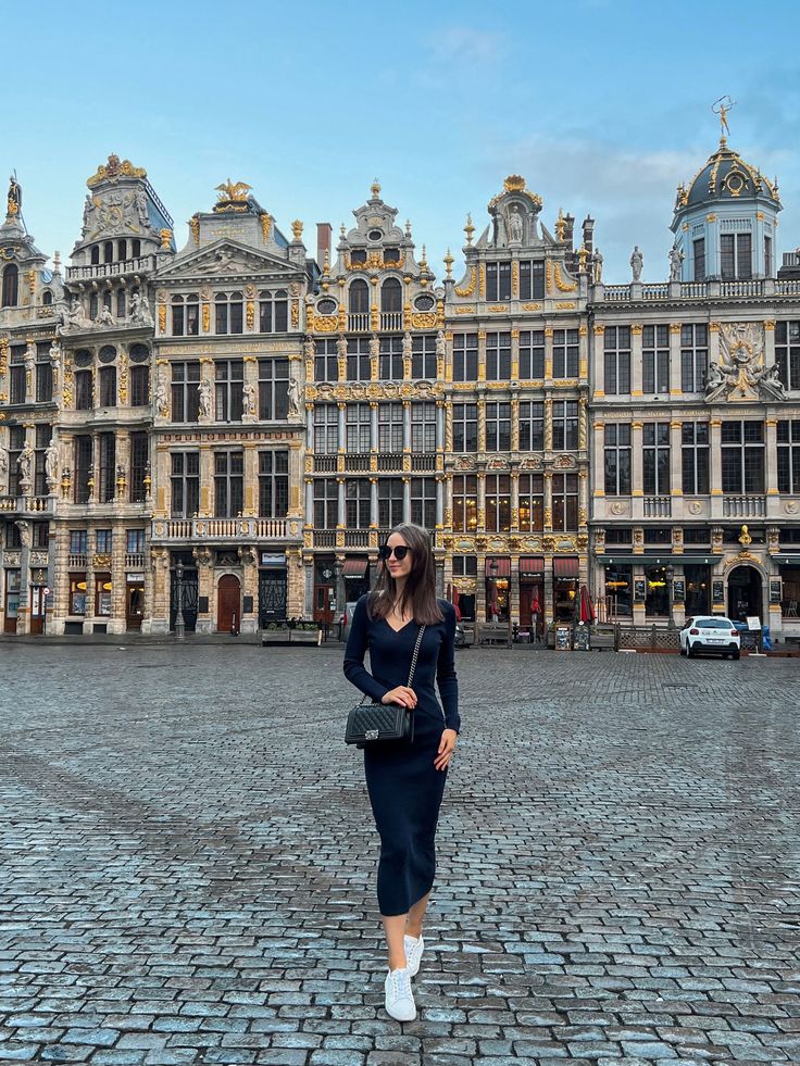 a woman standing in front of an old building with lots of windows and gold trim