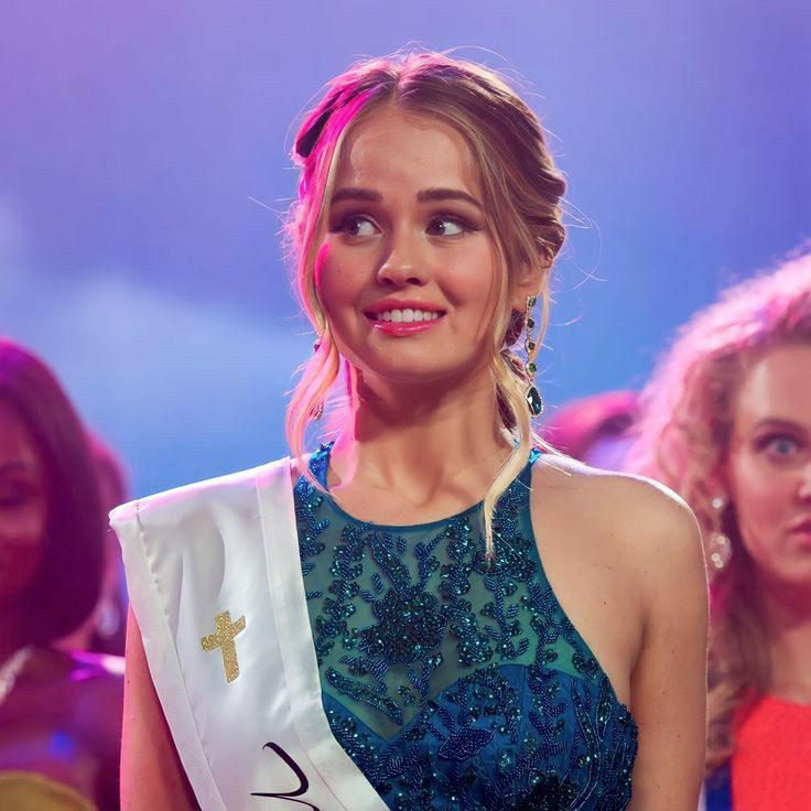 a woman in a blue dress is smiling at the camera while other women stand behind her