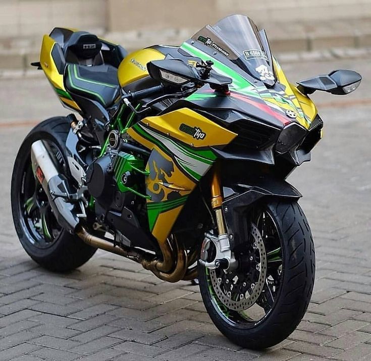 a yellow and green motorcycle parked on top of a brick road next to a building