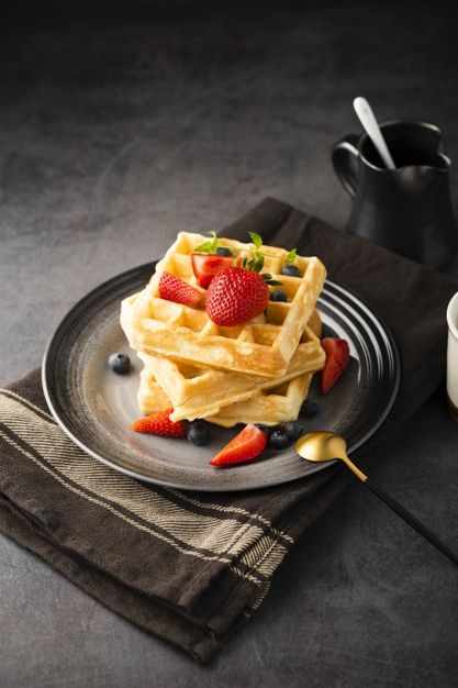 waffles with strawberries and blueberries on a plate next to a cup of coffee