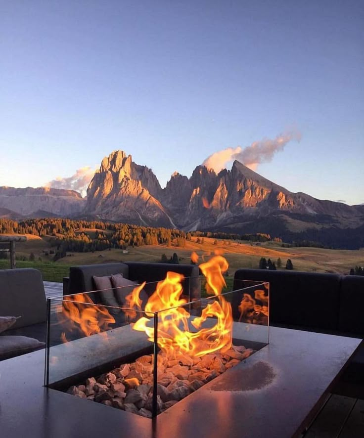 a fire pit sitting on top of a wooden table in front of mountains and grass