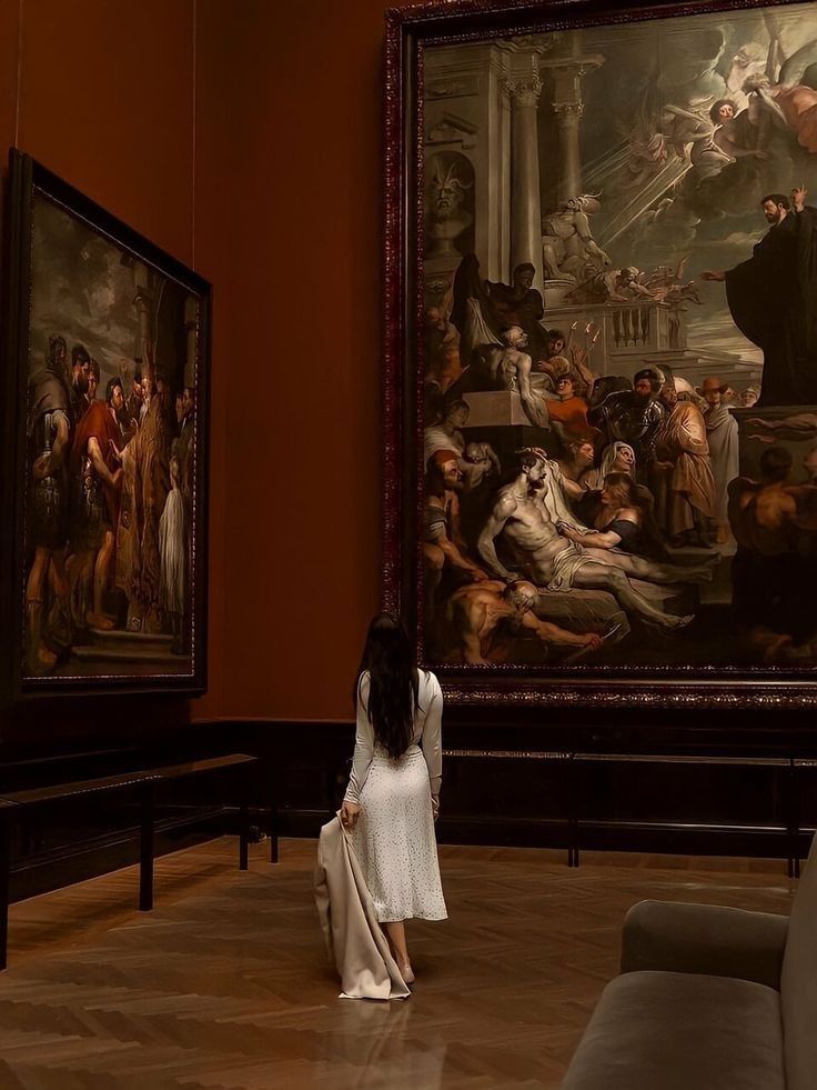 a woman is standing in front of two paintings on the wall and looking at them