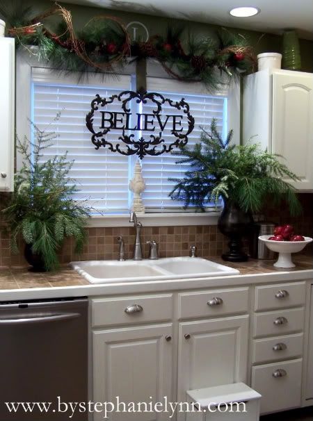 a kitchen decorated for christmas with wreaths and greenery on the window sill