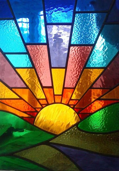 a colorful stained glass window with the sun setting in the center and green grass below