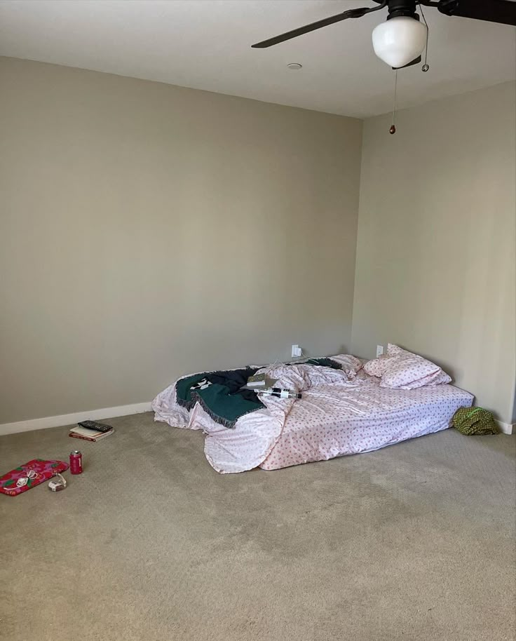 an unmade bed sitting in the middle of a room next to a ceiling fan