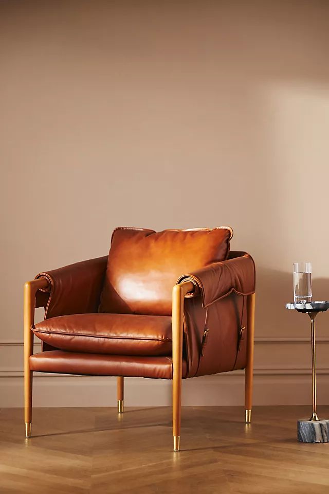 a brown leather chair sitting on top of a hard wood floor next to a lamp