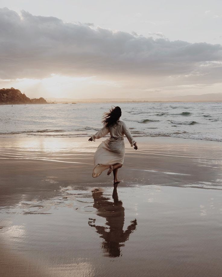 a woman is running on the beach at sunset