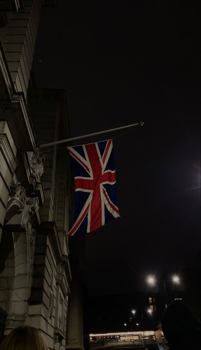 a british flag hanging from the side of a building at night with people walking by