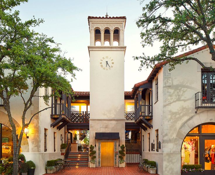 the clock tower is located in front of several buildings with trees and bushes around it