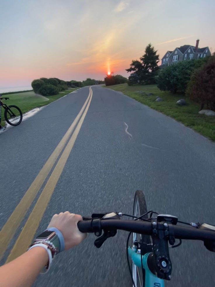 the person is riding their bike down the road with the sun setting in the background