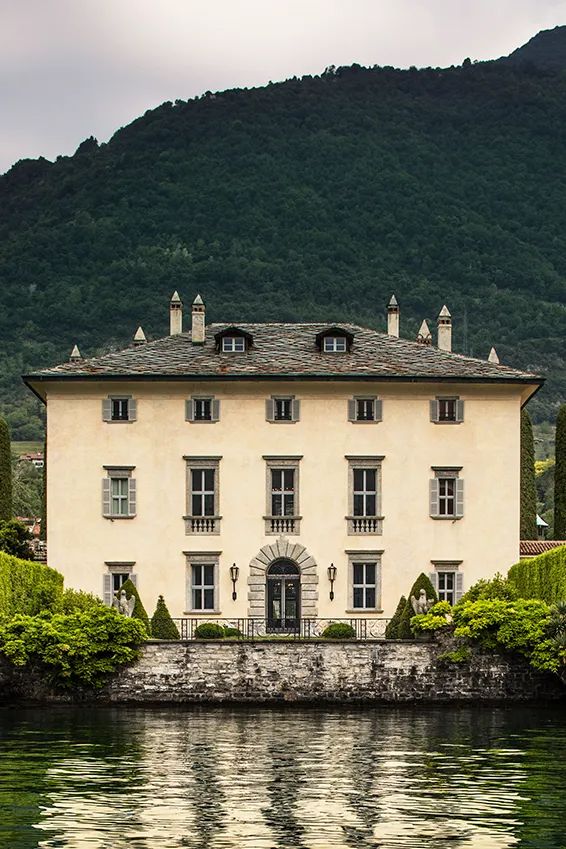 a large white house sitting on top of a lake next to a lush green hillside