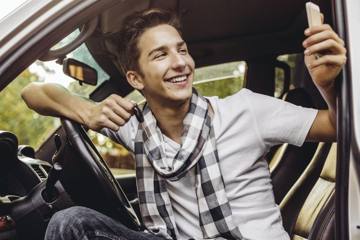 a man sitting in the driver's seat of a car holding up a cell phone