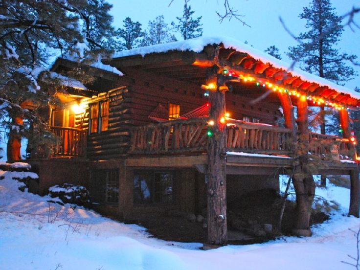 a log cabin covered in snow with christmas lights on the roof and porch railings