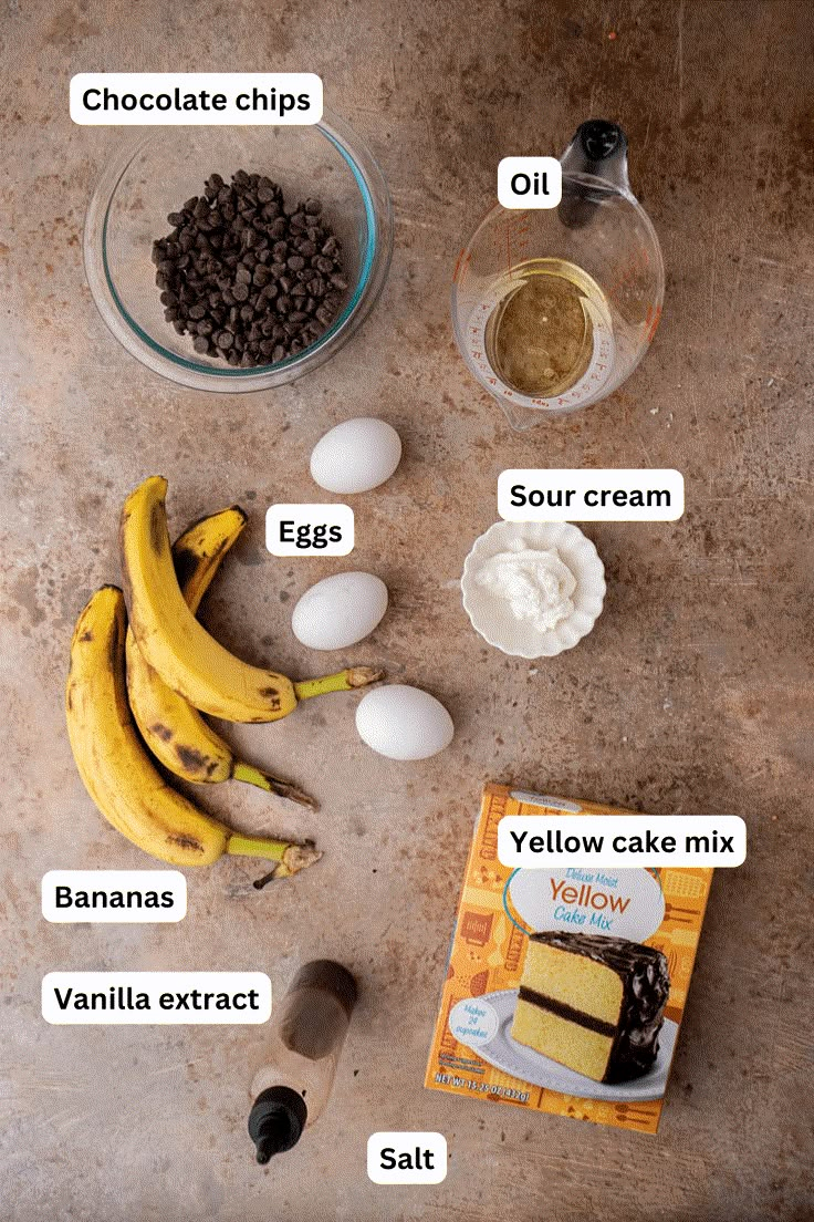 ingredients to make chocolate chip cake laid out on a table with eggs, bananas, and flour