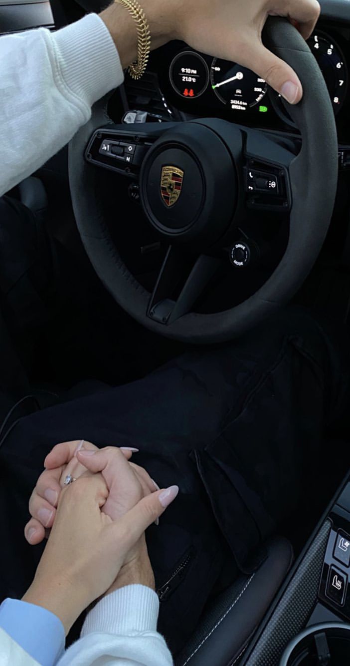 two people holding hands while sitting in a car with the driver's hand on the steering wheel