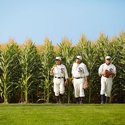 three baseball players standing in front of a corn field