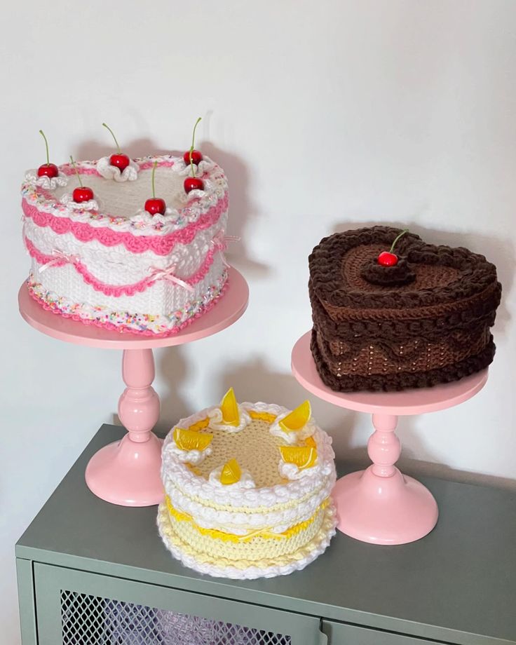 three cakes sitting on top of two pink pedestals next to each other in front of a white wall