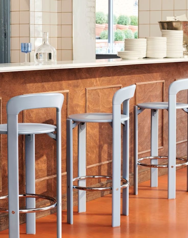 three stools in front of a counter with plates on it