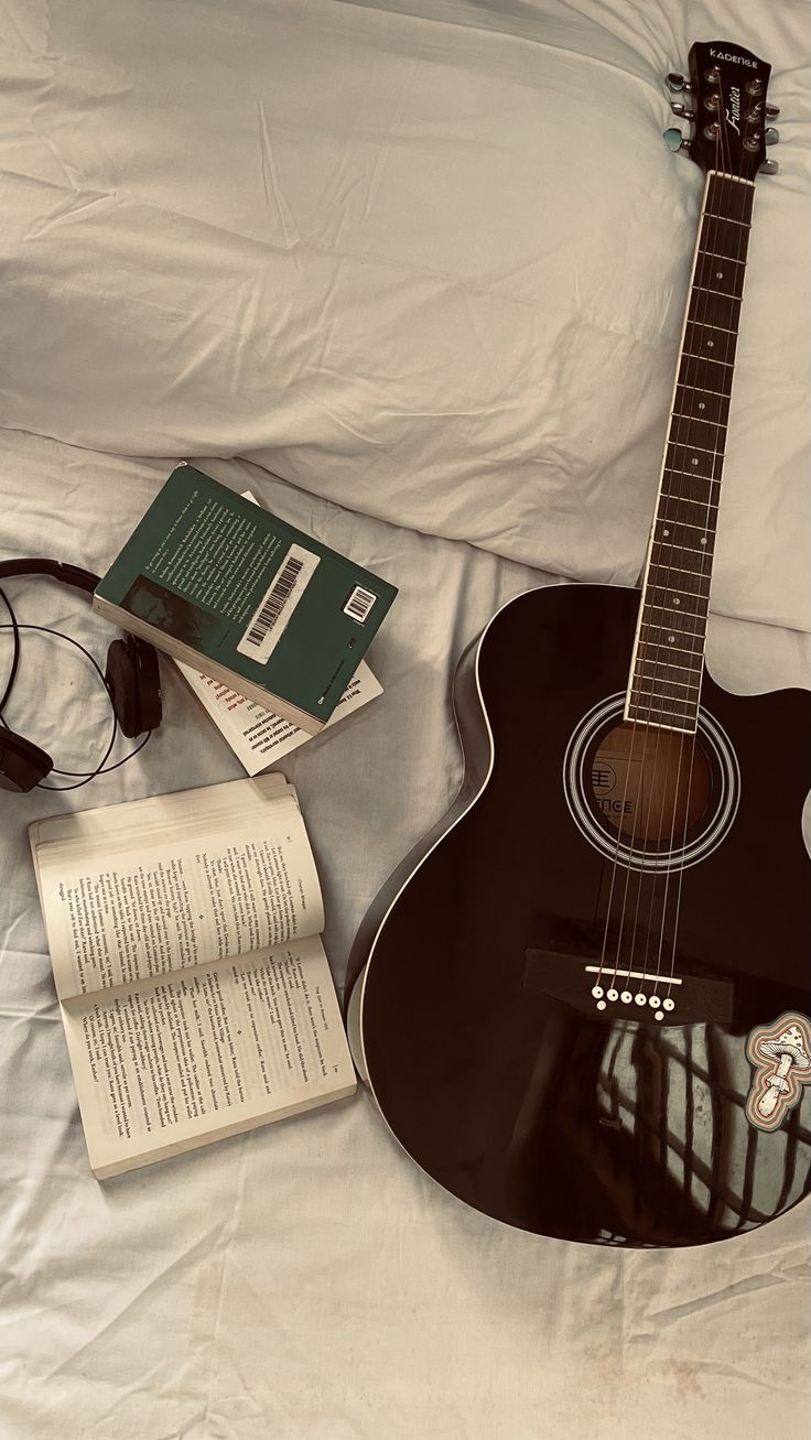 a guitar, book and headphones laying on a bed