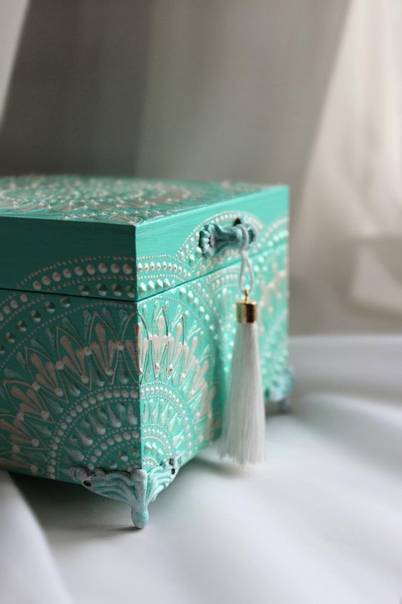 a decorative box with tassels on the lid sits on a white tablecloth