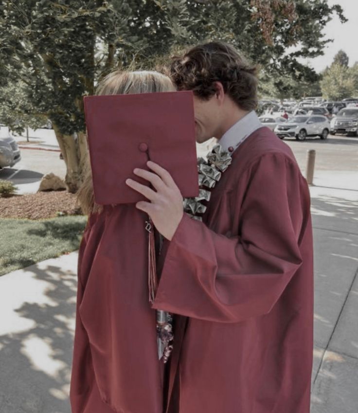 a man and woman in red graduation gowns kissing each other on the side walk