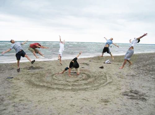 a group of people standing on top of a sandy beach next to the ocean with their arms in the air