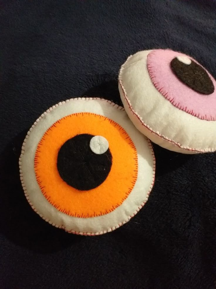 two pillows that have been made to look like eyeballs on black fabric with white and orange trim