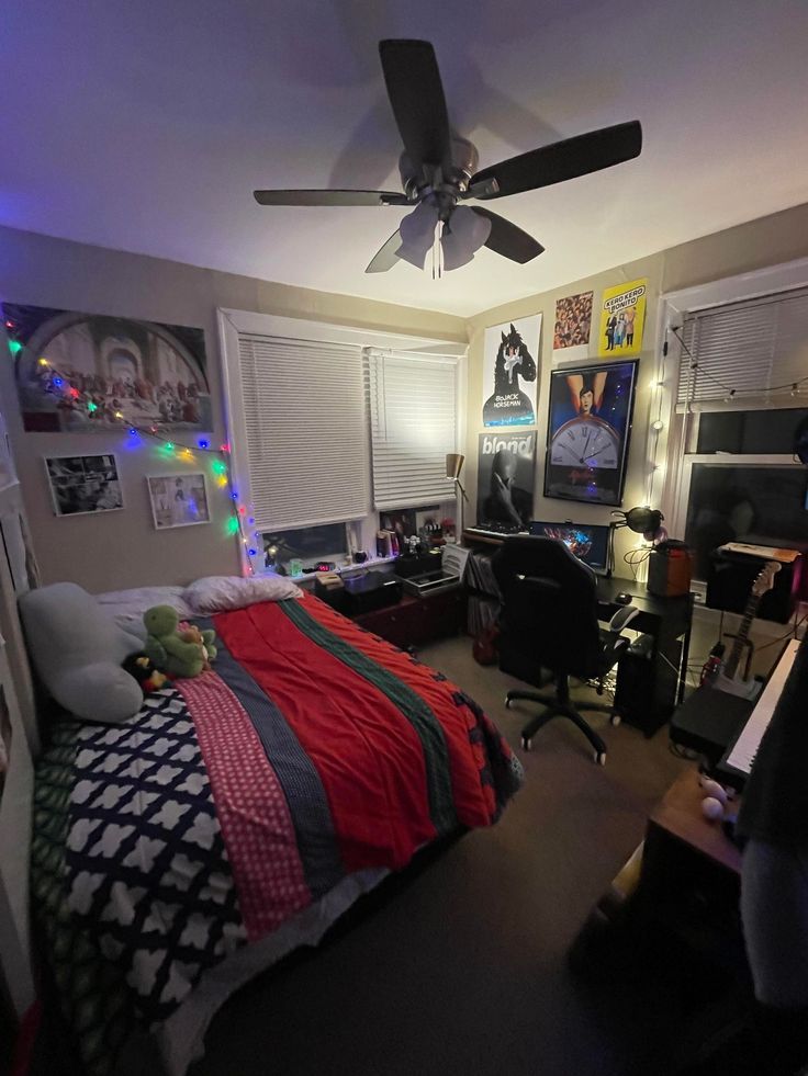 a bedroom with a bed, desk and ceiling fan in the corner is lit up by colorful lights