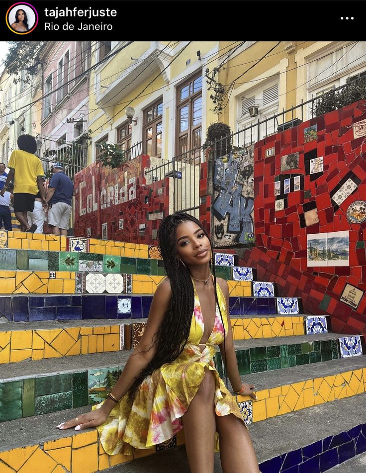 a woman in a yellow dress sitting on some steps with colorful tile walls behind her