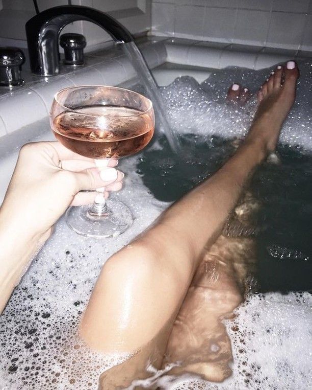 a person laying in a bathtub with a glass of wine next to their feet