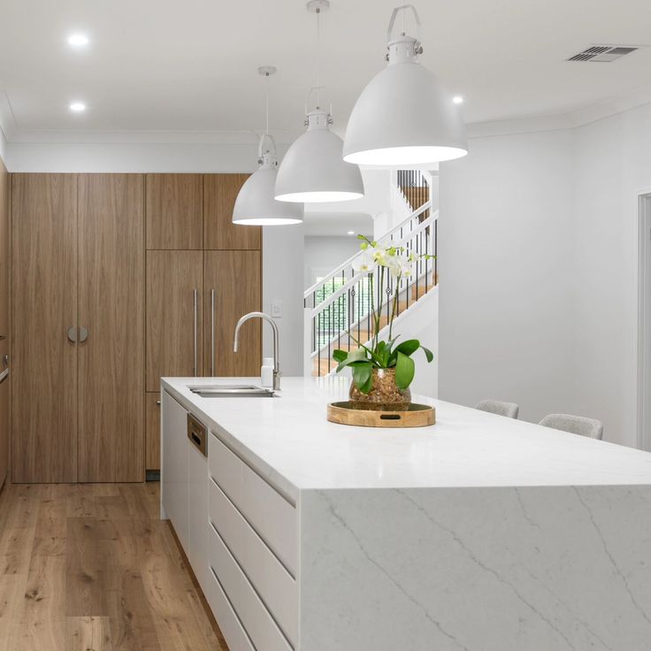 a kitchen with white counter tops and wooden cabinets, along with hanging lights over the island