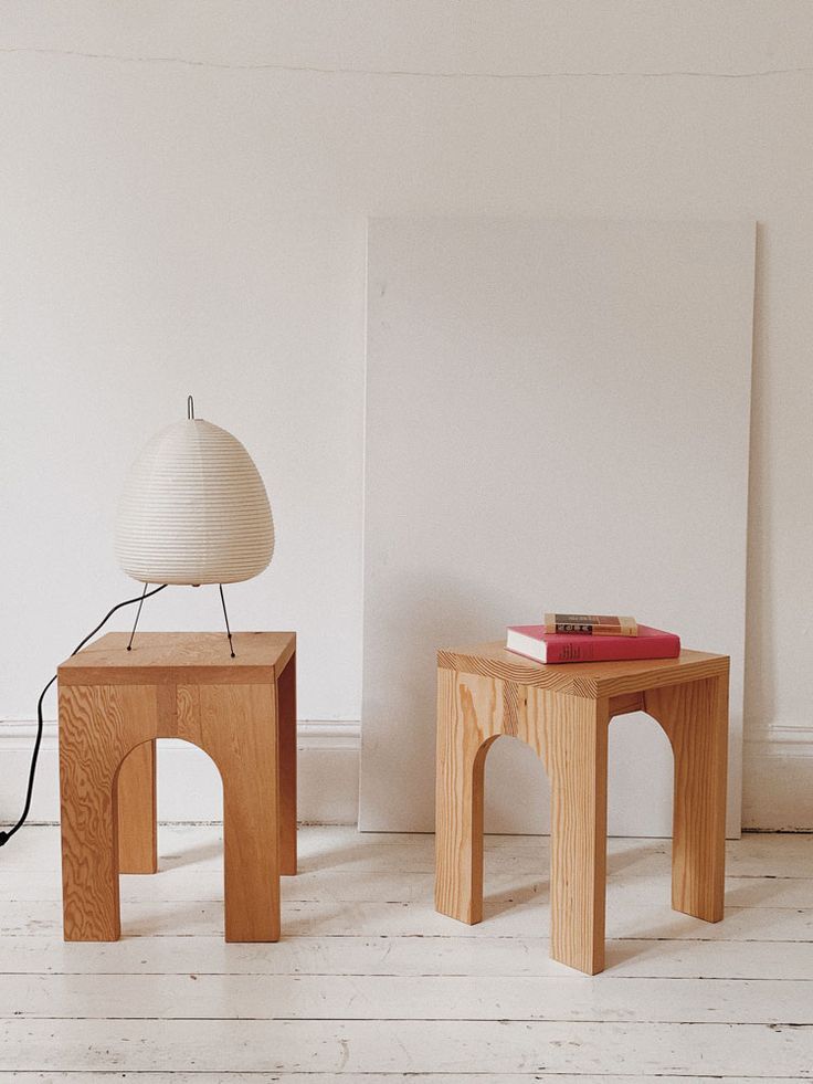 two wooden tables with books on them in front of a white wall and floor lamp