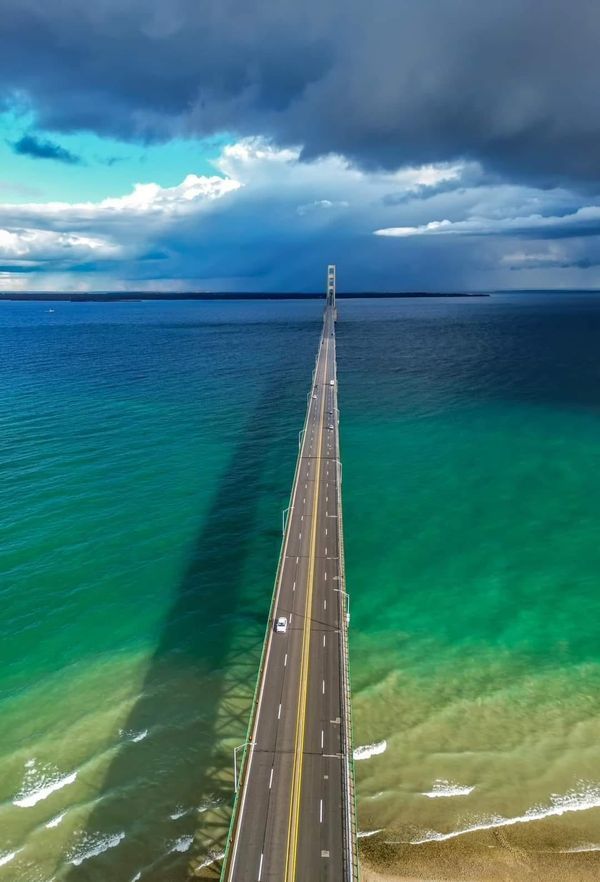 an aerial view of a long bridge over the ocean with cars driving on it and dark clouds in the sky