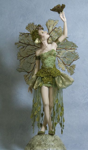 a woman dressed as a leaf fairy holding a flower in her right hand and looking up at the sky