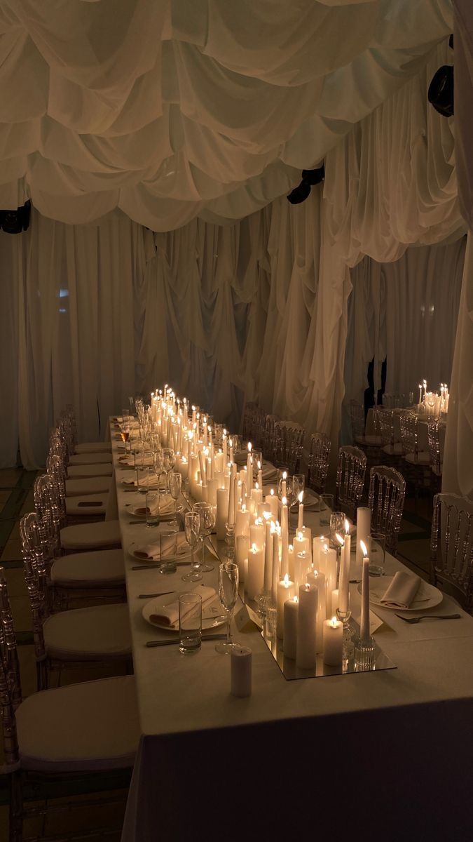 a long table with many lit candles on it in front of white draping