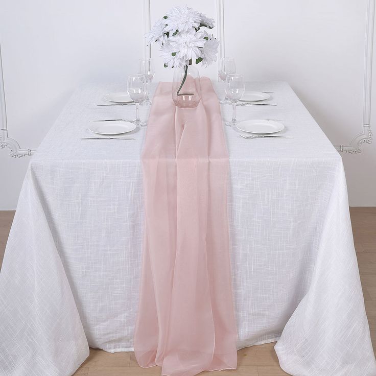 a white table topped with a vase filled with flowers next to two plates and glasses