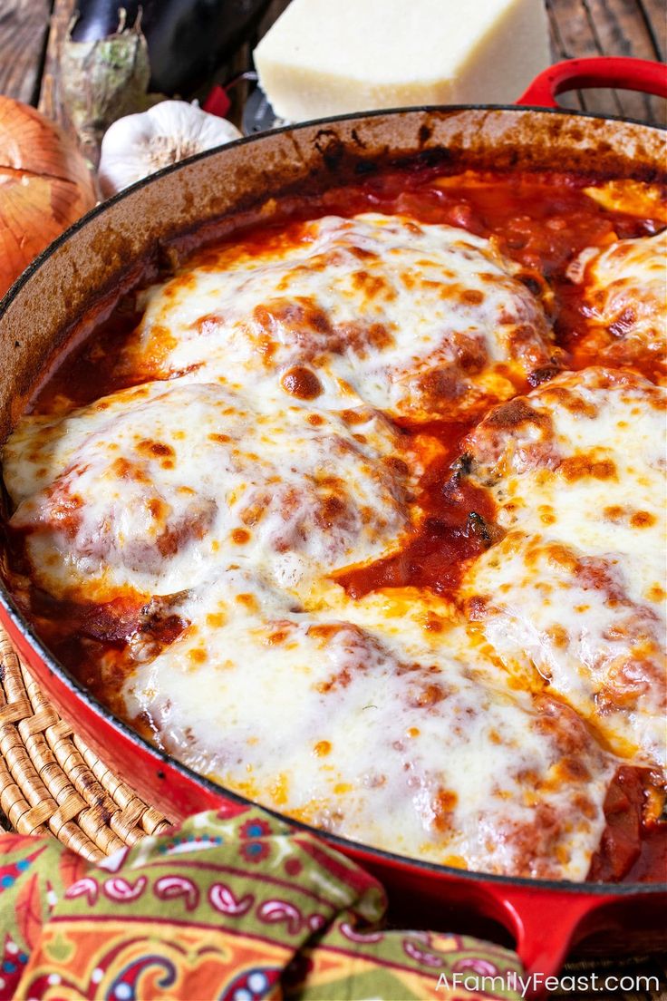 a pizza in a red pan with cheese on top next to some bread and garlic