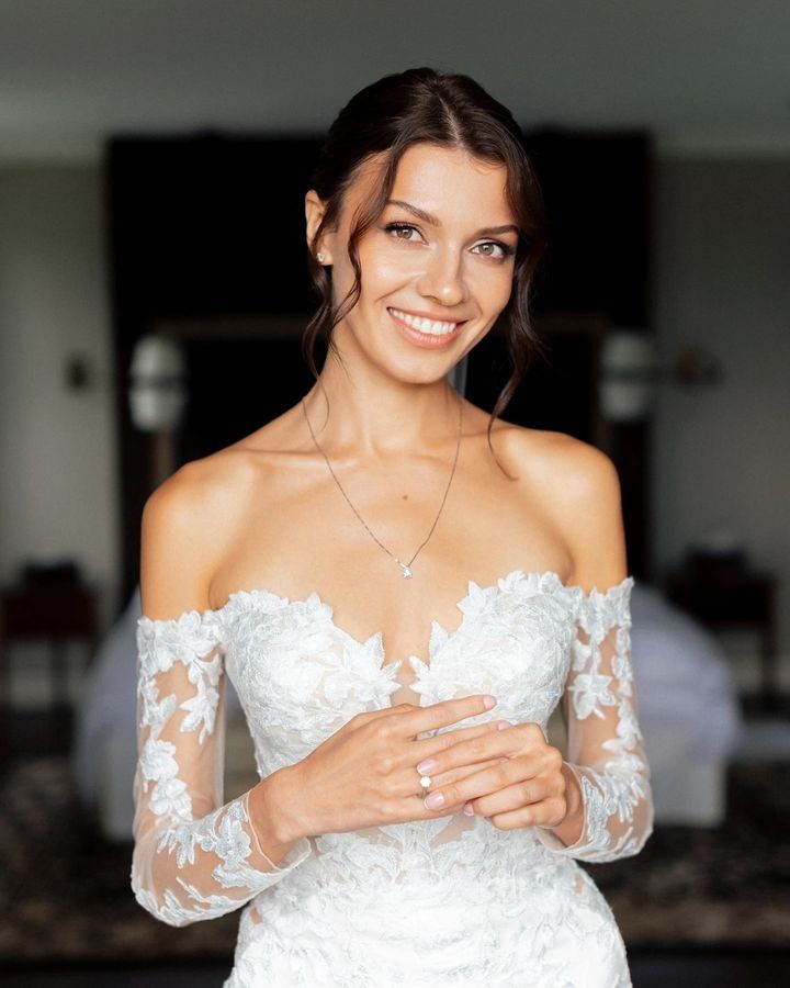 a woman in a wedding dress smiling and holding her hands on her chest while wearing a diamond necklace