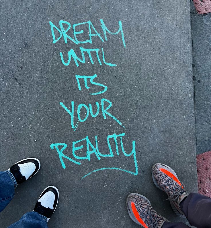 two people standing in front of a chalk drawing that says dream until it's your reality