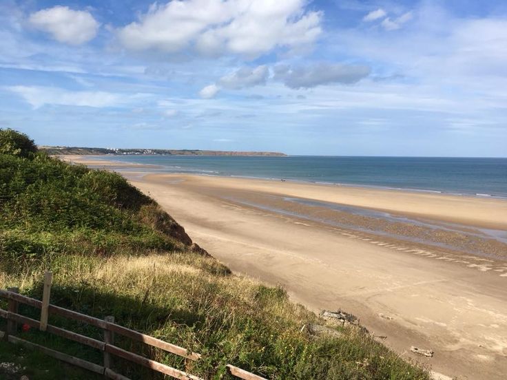 a sandy beach next to the ocean under a cloudy blue sky