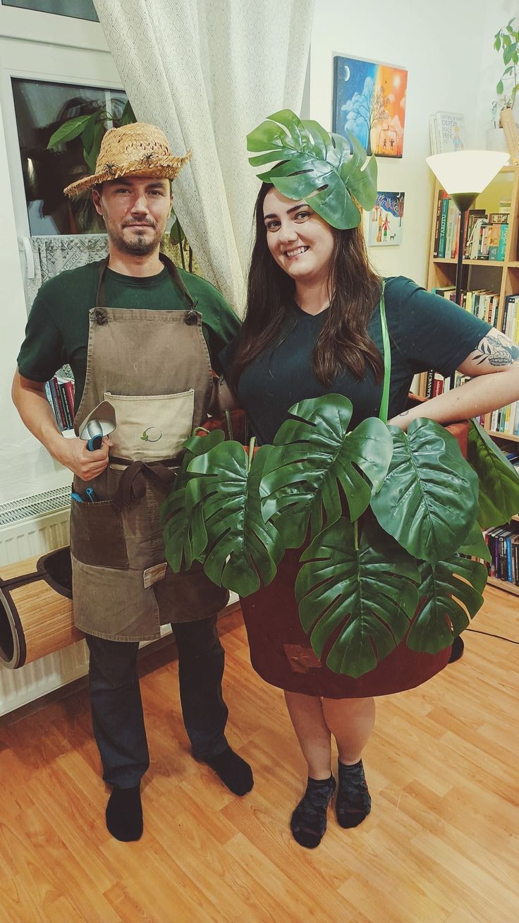 a man and woman are dressed up as plants in the kitchen, one is holding a potted plant