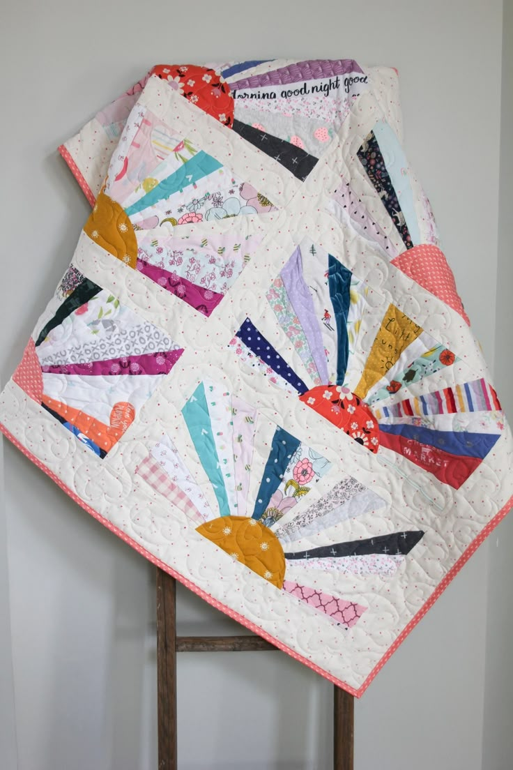 a quilted table topper is displayed on a wooden chair in front of a white wall