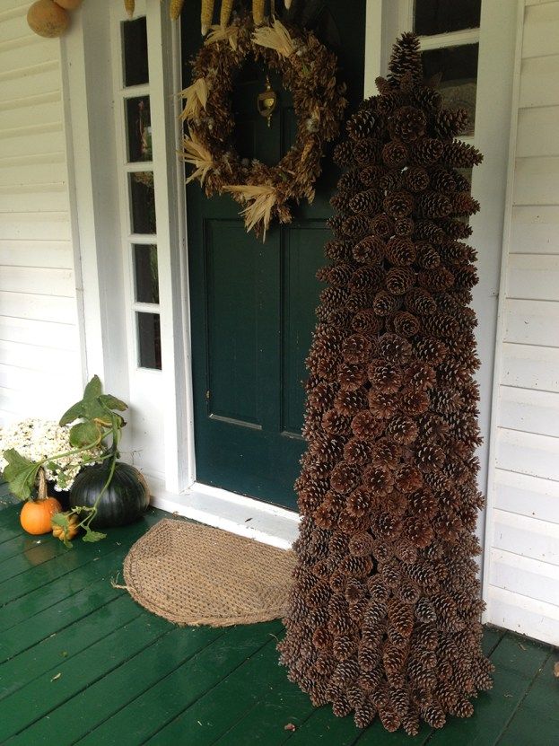 a tall pine cone is on the front porch with wreaths and pumpkins around it