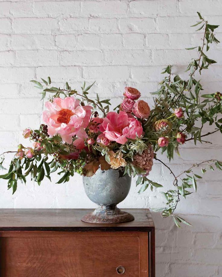 a vase filled with pink flowers sitting on top of a wooden dresser next to a brick wall