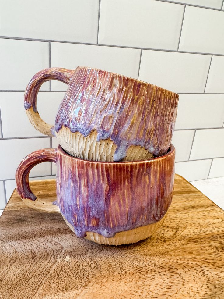 two coffee mugs sitting on top of a wooden table next to a white brick wall