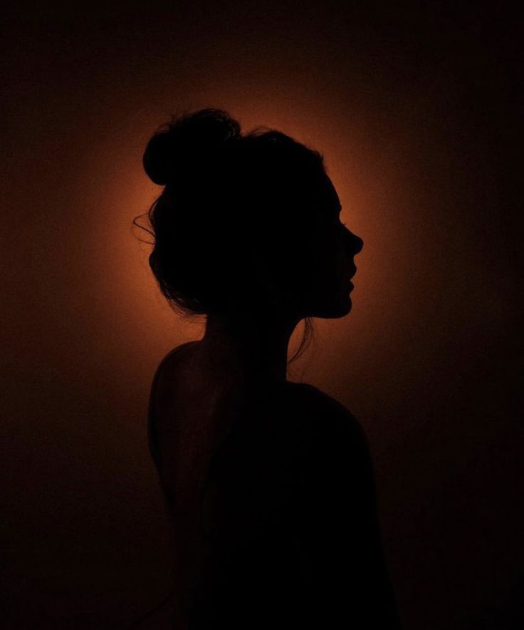 the silhouette of a woman's head is shown against a dark background with orange light